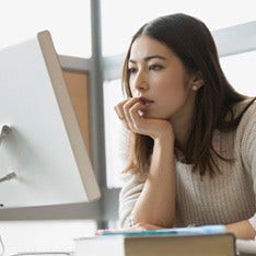 A young woman is looking intently at her desktop monitor.