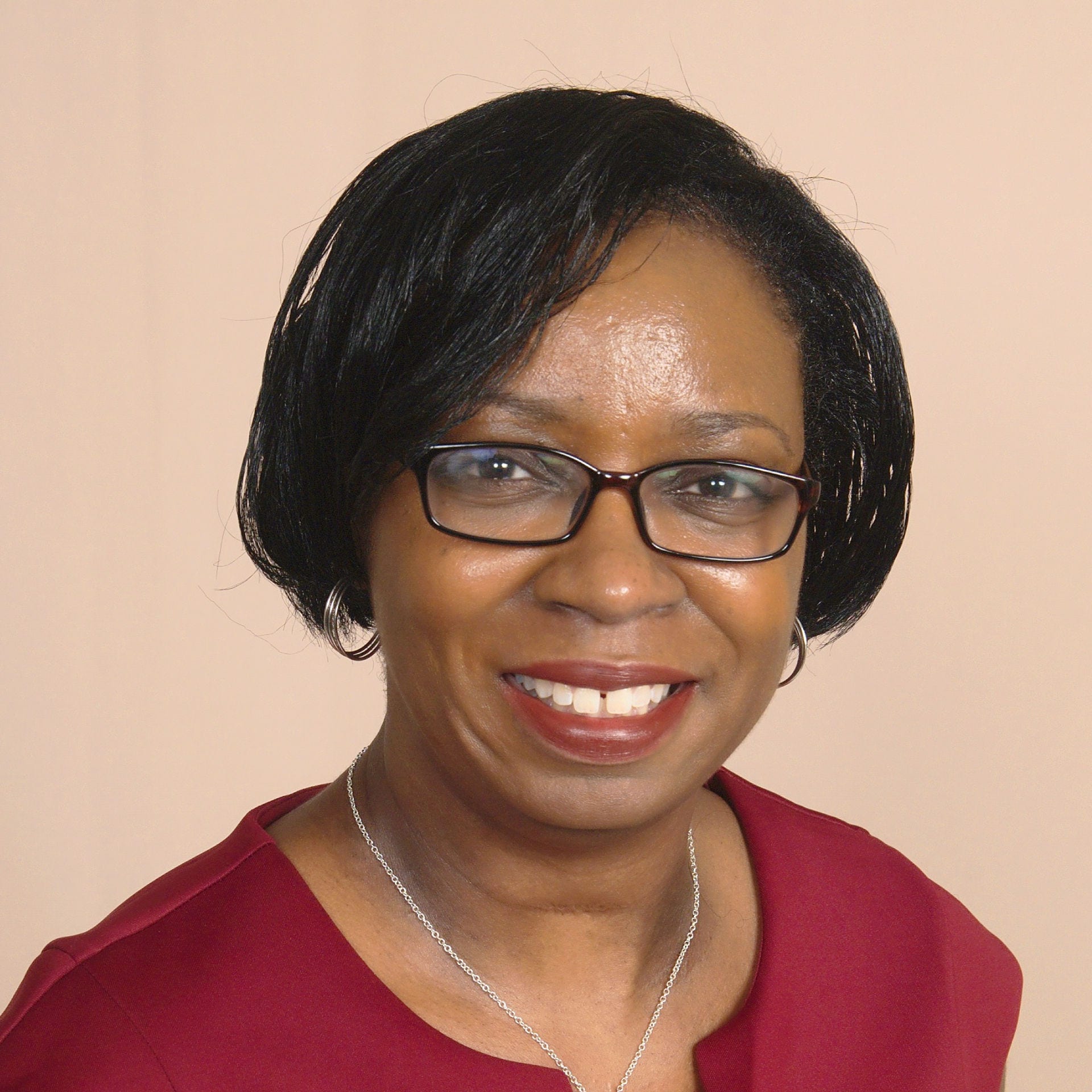 black woman with glasses in red, zippered dress and silver cross necklace