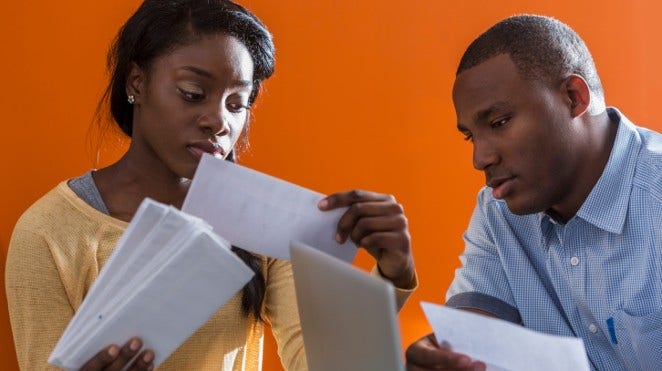 a worried young couple sits at computer going through their bills