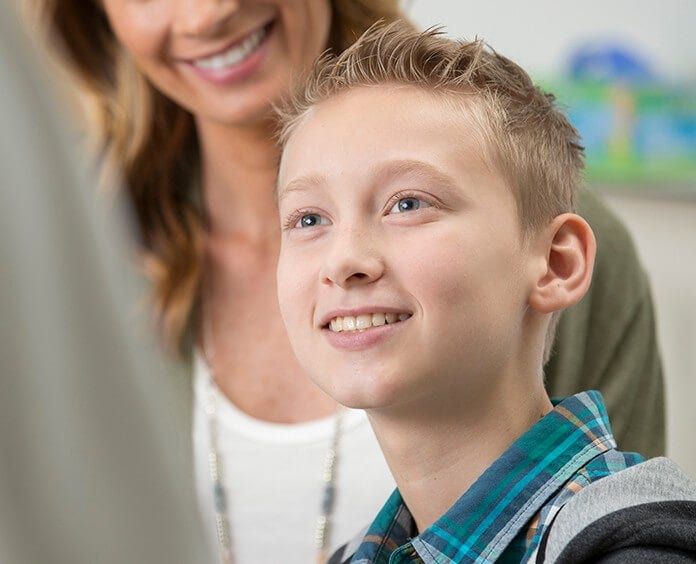 Caucasian, young male smiling at the doctor while mother stands behind him