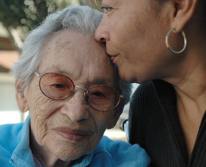 young woman kissing elderly woman on forehead