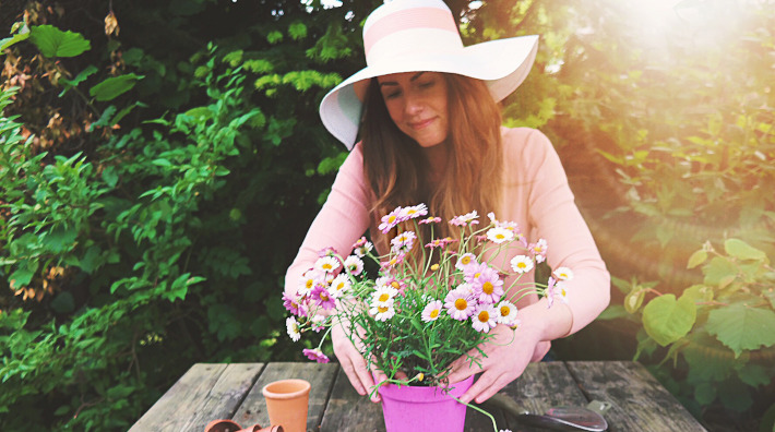 woman in wide brimmed hat potting flowers outside